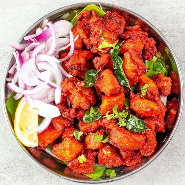 Madurai Kitchen and Bar's Chicken 65, a vibrant red fried chicken dish with onions and lemon.