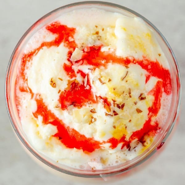 Overhead view of a glass of Indian falooda, with white ice cream, red syrup, and nuts.