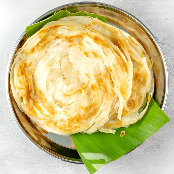 Golden-brown, flaky Indian parotta bread served on a banana leaf in a silver plate.