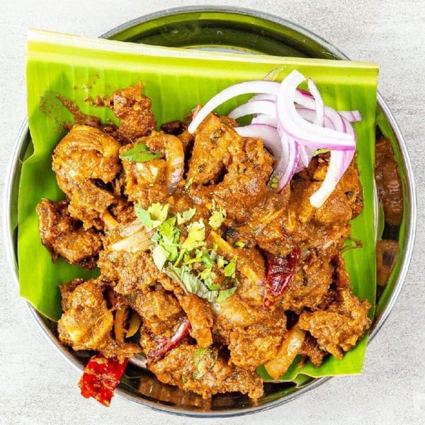 Madurai Kitchen and Bar's Indian chicken dish, garnished with red onions and cilantro on a banana leaf.