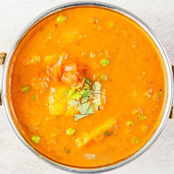 Overhead view of a vibrant orange Indian curry with peas, potatoes, and cilantro in a metal bowl.