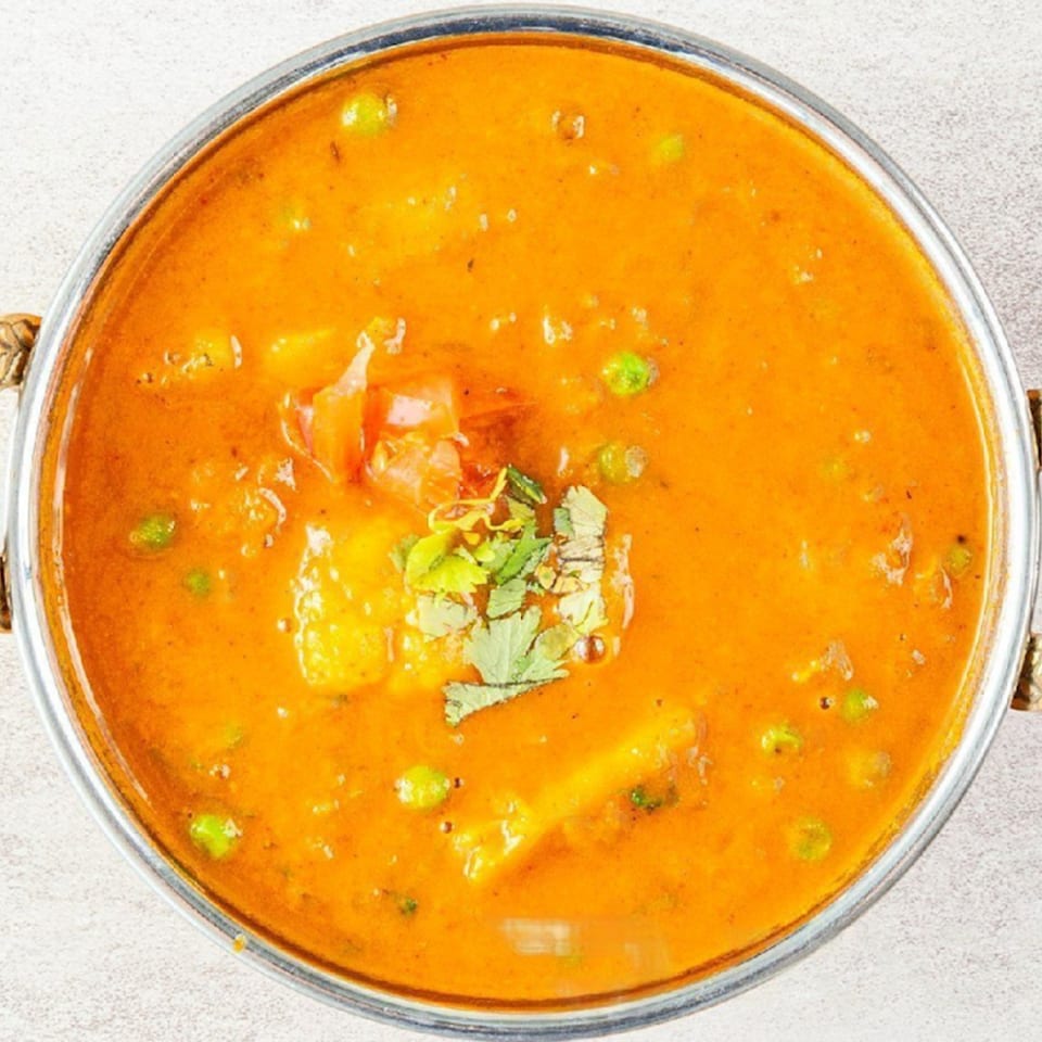 Overhead view of a vibrant orange Indian curry with peas, potatoes, and cilantro in a metal bowl.